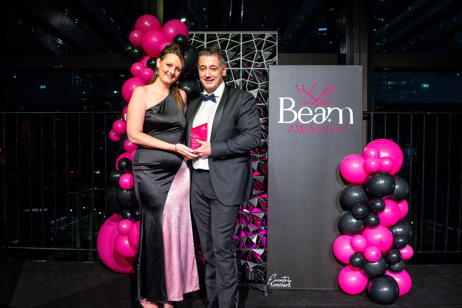 A Beam Awards gold winner presented with their trophy in front of the Beam media wall